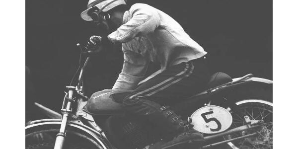 Auf diesem Bild sehen Sie einen Mann auf einem Husqvarna Motorrad. Das Bild ist in schwarzen und weißen Farben gehalten.